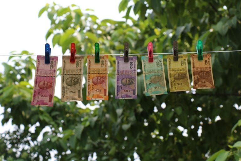 Indian currency notes clipped to a clothesline, hanging against a backdrop of lush green trees